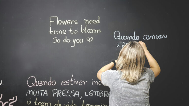 A student writing multilingual sentences on a chalkboard, showing the advantages and disadvantages of bilingual education.